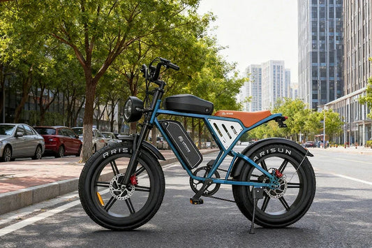 Blue vintage-styled Jansno X70 Pro electric cruiser fitted with orange leather seat and ARISUN thick fat tyres, stationary on urban asphalt beside green trees and modern high-rise buildings