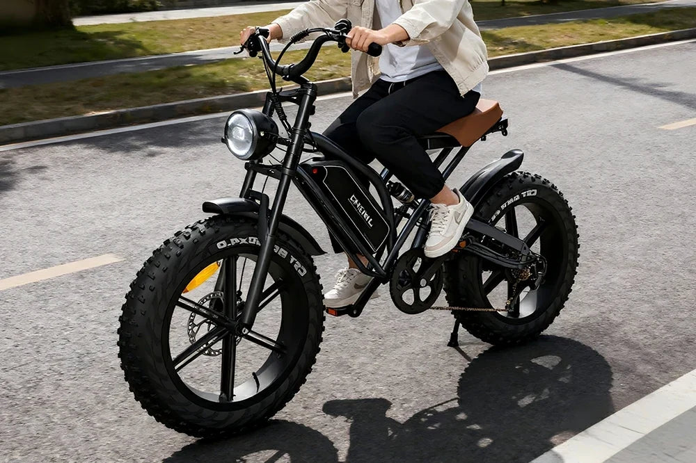 Sunny suburban road lifestyle shot of a rider cruising matte black retro Jansno X50 fat tire e-bike with tan leather saddle and vintage round headlight on smooth asphalt street.