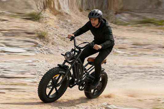 Dynamic off-road action shot of rider in black gear riding retro matte black Jansno X50 fat tire electric bike over rocky desert trail.