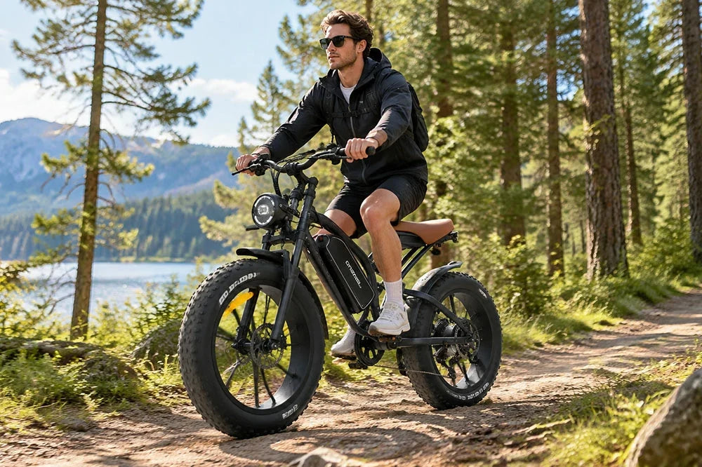 Man riding Jansno X50 fat tire electric bike on forest trail with lake and mountain scenery.