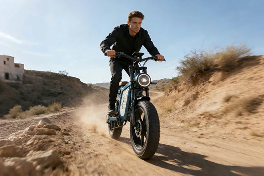 Dynamic low-angle action shot of male rider speeding matte blue Jansno X60 retro fat tire e-bike kicking up dust on sunlit desert dirt trail.