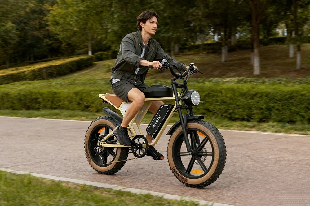 Young man riding retro‑style Jansno X70 fat‑tire e‑bike along sunlit park paved trail.
