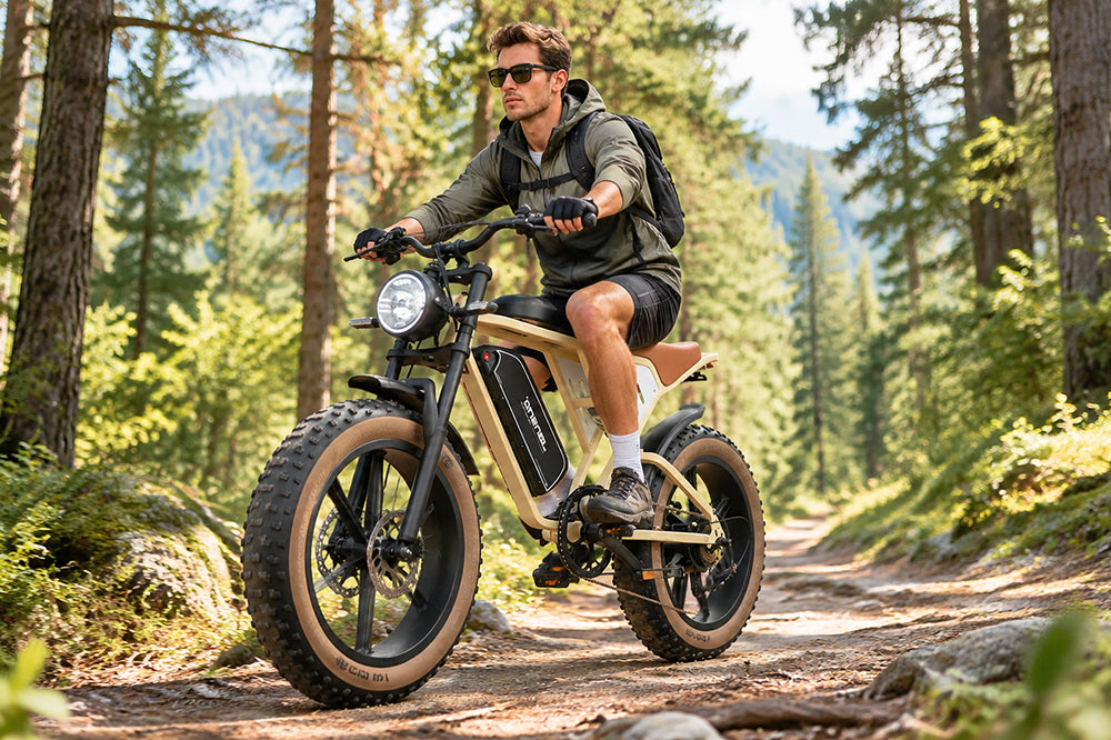 Man riding Jansno X70 retro fat tire electric bike on sunlit forest trail with mountain scenery.