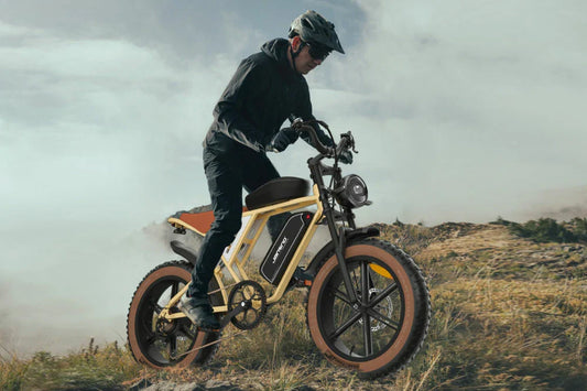 Dynamic misty hillside action shot of helmeted male rider traversing rugged grassy highland trails on cream retro-styled Jansno X70 fat tire electric bike.